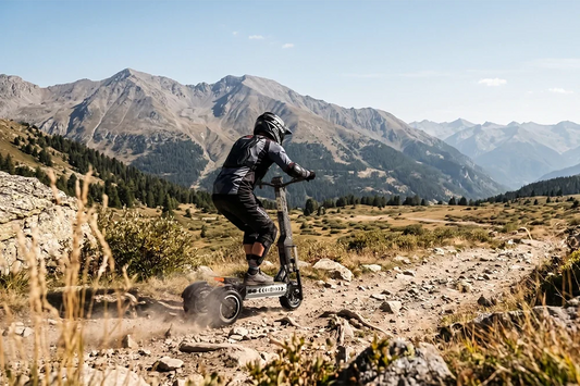 Back view of rider riding OOTD T30 heavy-duty off-road electric scooter on rocky alpine trail, wide mountain range landscape, outdoor exploration