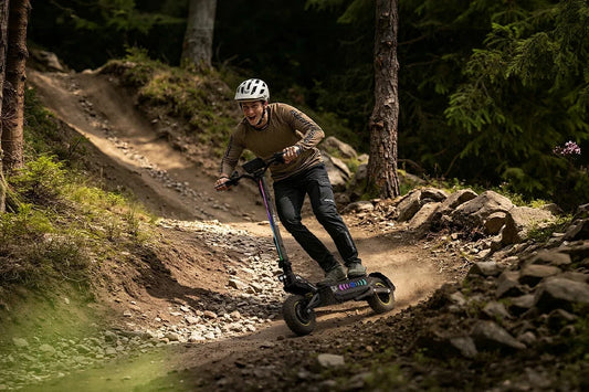 Male rider with helmet riding RGB lighted off‑road electric scooter on rough mountain dirt trail, extreme outdoor sport e‑scooter